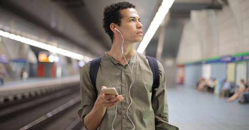 Underground Music - Young ethnic man in earbuds listening to music while waiting for transport at contemporary subway station