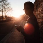Sunset Views - Boy Standing Near Wall Holding Smartphone While Looking Sideways
